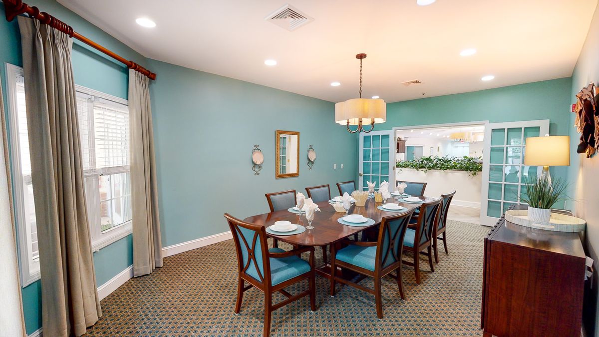 A well-lit dining room with a large table set for a meal, surrounded by chairs and featuring blue painted walls.