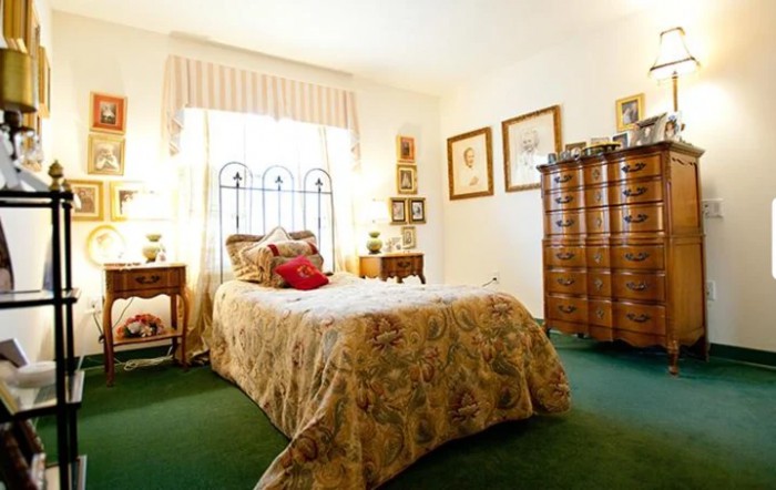 A cozy bedroom with classic decor, featuring a bed, dresser, and vintage-style furnishings.