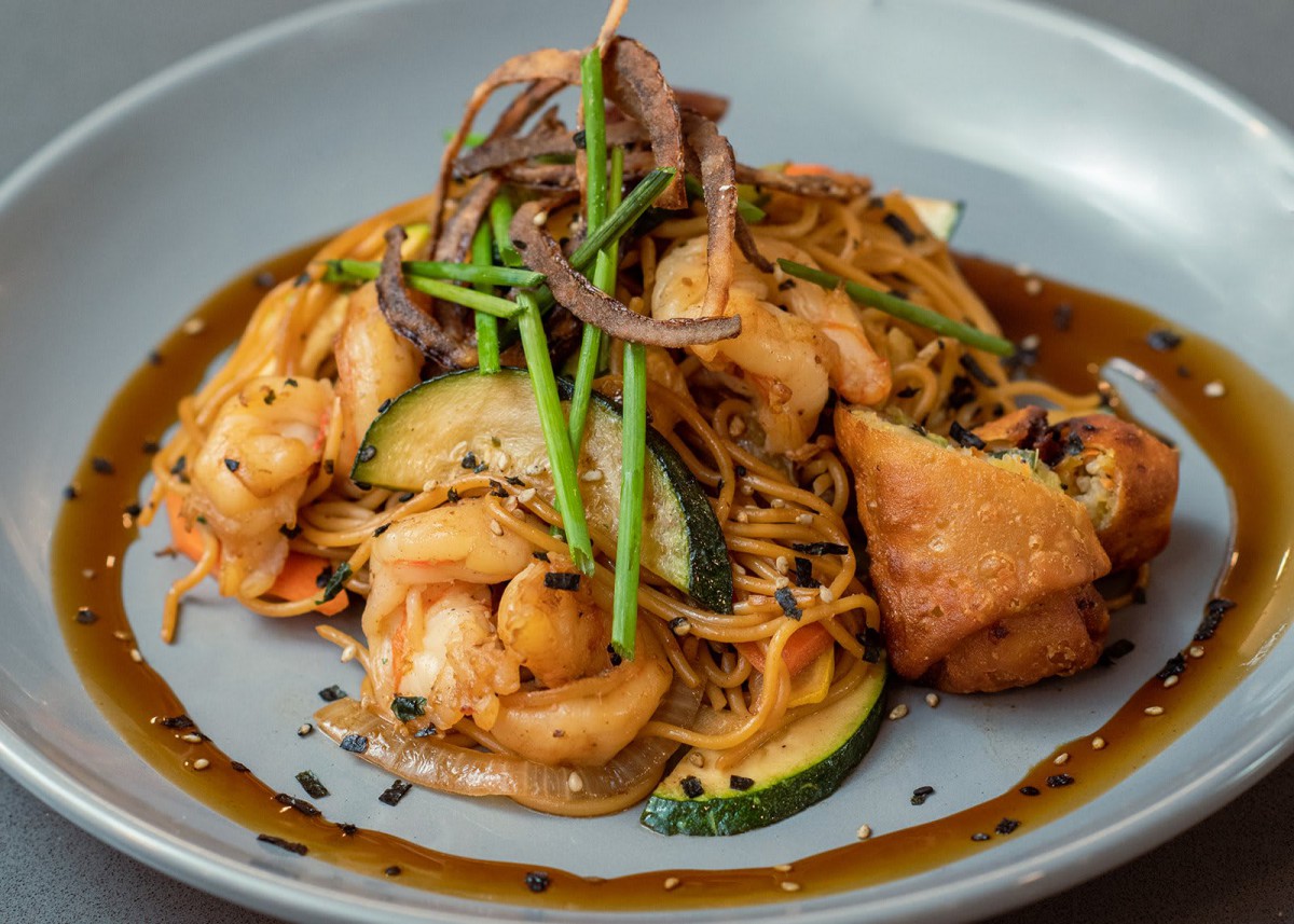 A delicious plate of noodles topped with shrimp, tofu, and vegetables, garnished with herbs.
