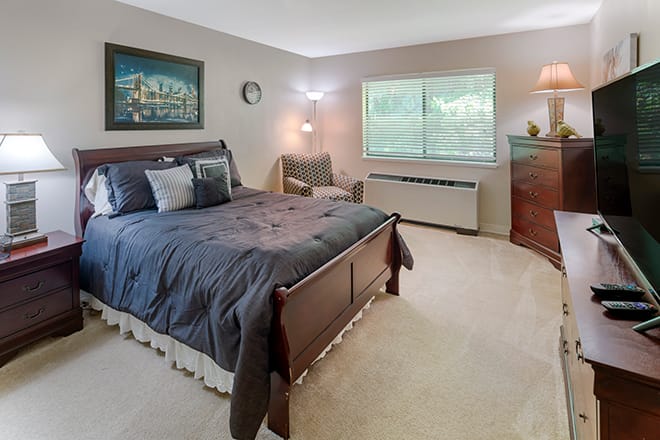 A cozy bedroom with a large bed, armchair, and dresser under natural light.