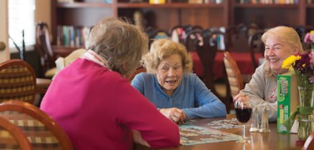 Two elderly women engaged in conversation while working on a puzzle together.