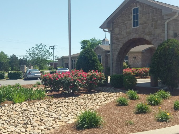 A sunny day view of a stone building with landscaped grounds and shrubs.