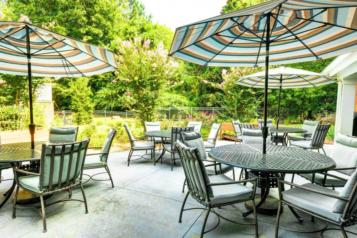 A serene patio with tables, chairs, and umbrellas set amidst lush greenery.