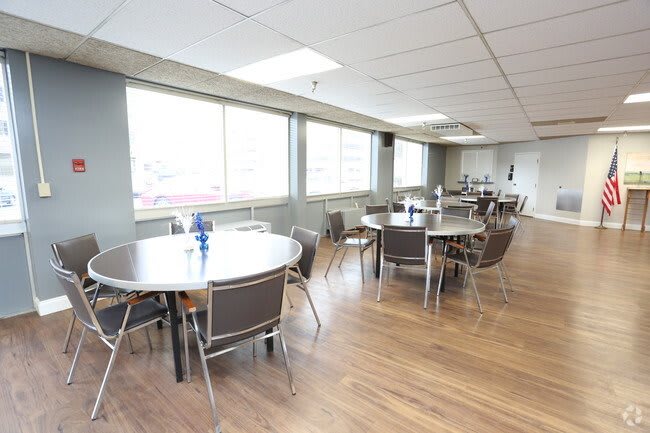 An empty cafeteria with round tables and chairs, featuring large windows that let in natural light.