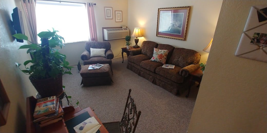 A cozy living room with a sofa, armchair, and coffee table, warmly lit by a lamp near the window.