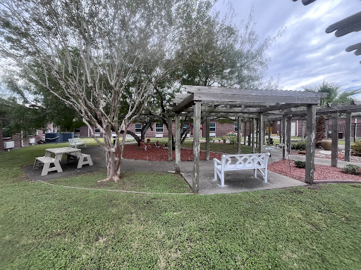 A tranquil outdoor space featuring a seating area under a pergola surrounded by lush greenery.