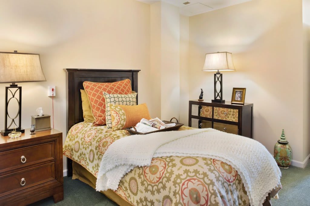 A cozy bedroom with a patterned bedspread and decorative pillows, featuring a nightstand and lamp.