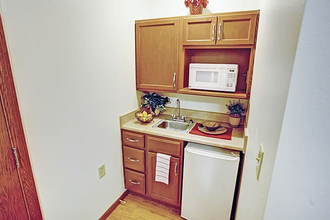 A compact kitchenette featuring a microwave, mini fridge, sink, and wooden cabinetry.