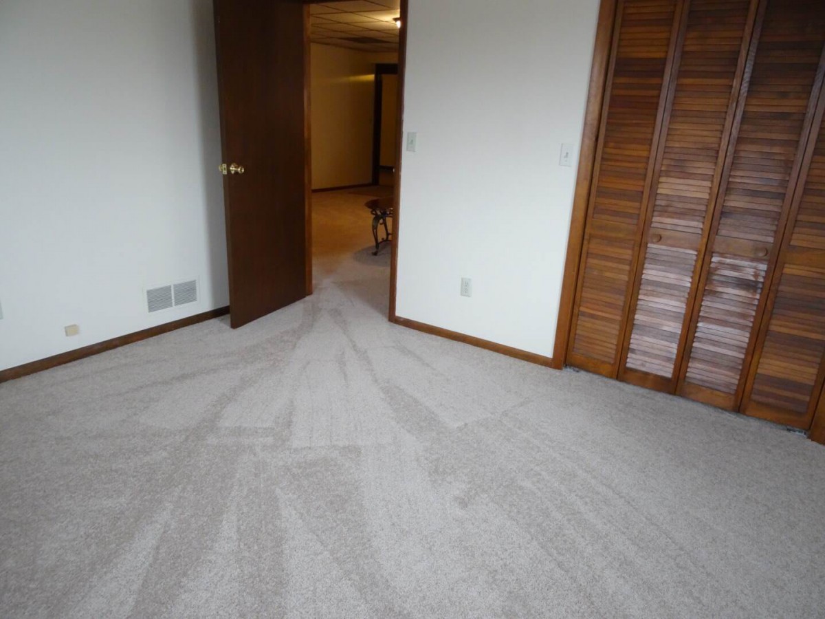 An empty room with freshly vacuumed carpet, an open door, and a wooden closet.