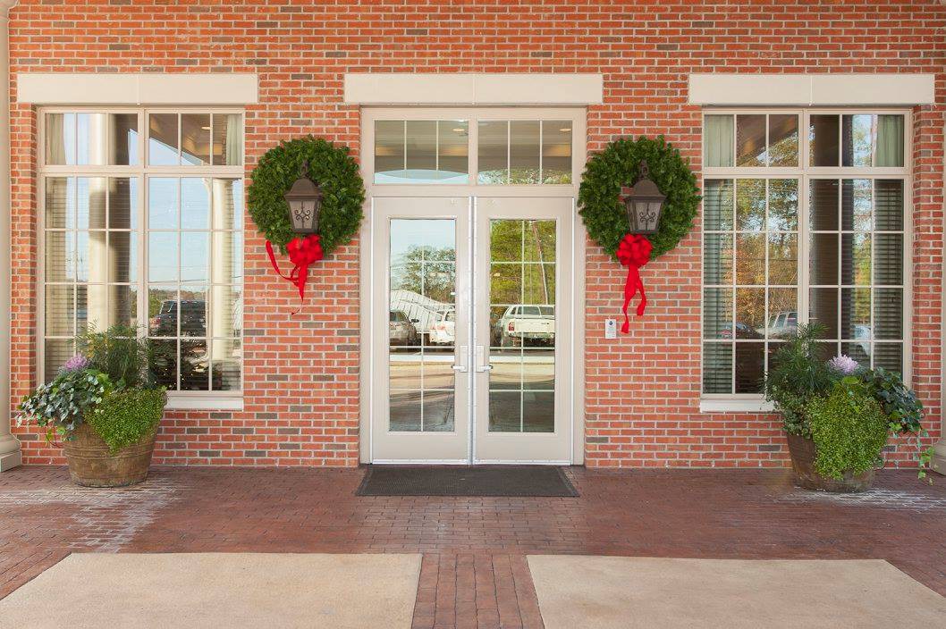A festive brick building entrance decorated with wreaths and red ribbons.