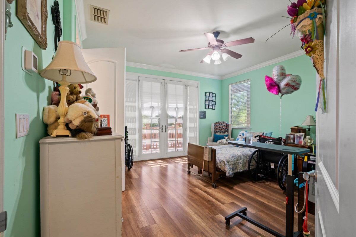 A cozy bedroom with wood flooring and wheelchair accessibility, featuring a ceiling fan and French doors leading outside.