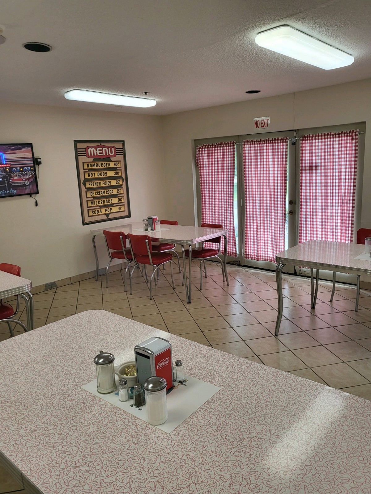 An empty diner with several tables and chairs arranged neatly, featuring pink curtains on the windows.