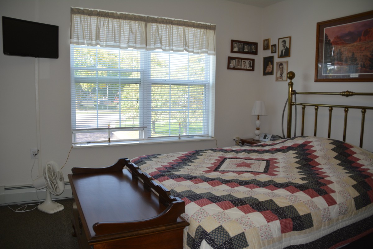 A cozy bedroom with a quilt-covered bed and large window providing natural light.