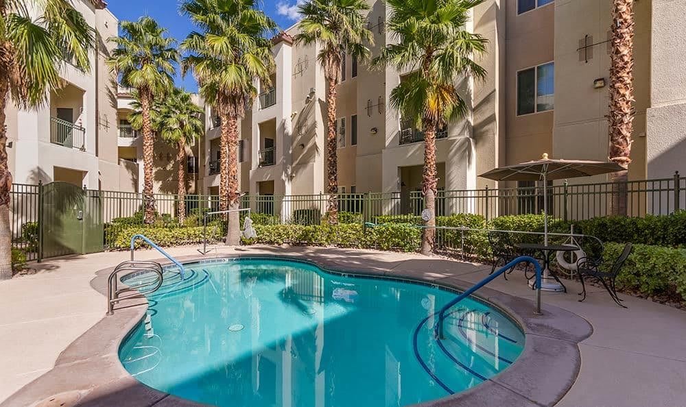 A serene outdoor swimming pool surrounded by palm trees and an apartment complex.