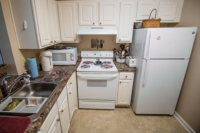 A compact kitchen featuring white cabinets, a stove with an oven, a microwave, and a refrigerator.