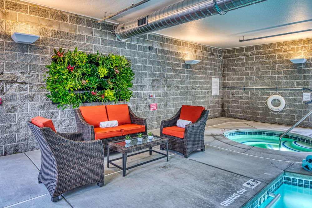 Indoor seating area with rattan chairs and a hot tub, featuring vibrant orange cushions and a vertical garden on the brick wall.