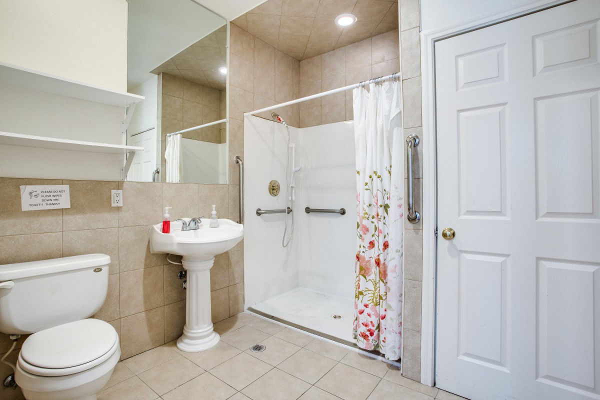 A clean and modern bathroom featuring a shower with a curtain, pedestal sink, and tiled floor.