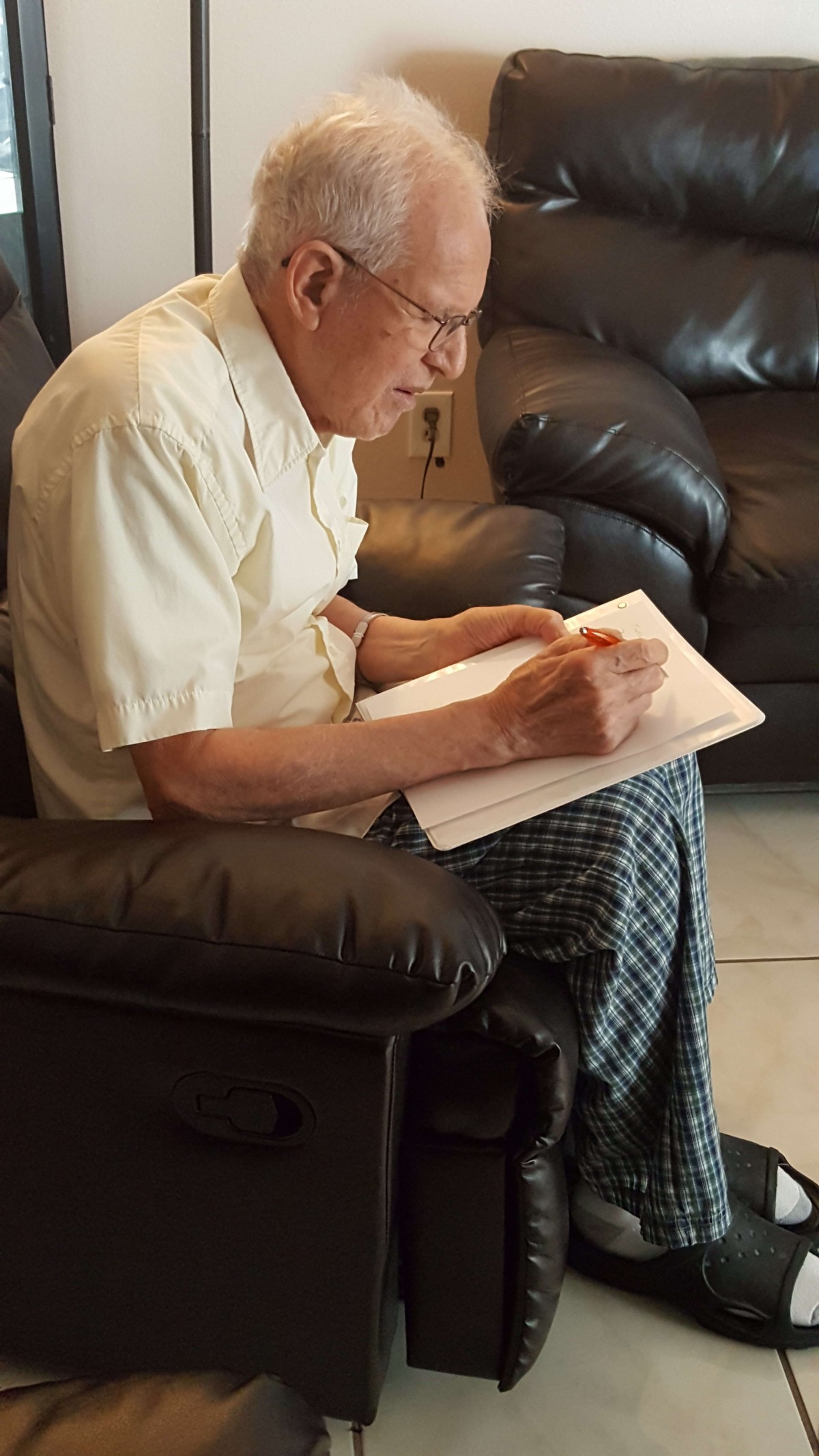 An elderly person writing in a notebook while sitting on a leather chair.