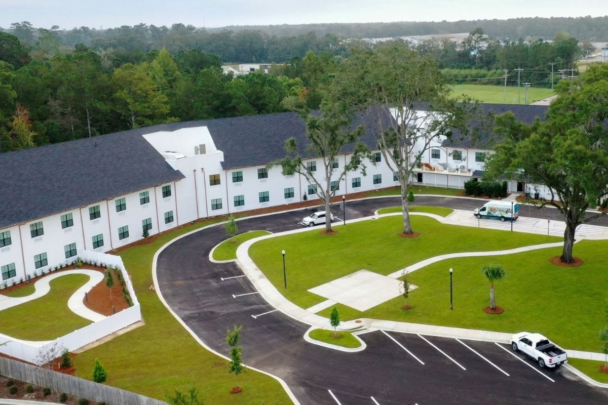 Aerial view of a white building with a parking lot surrounded by greenery.