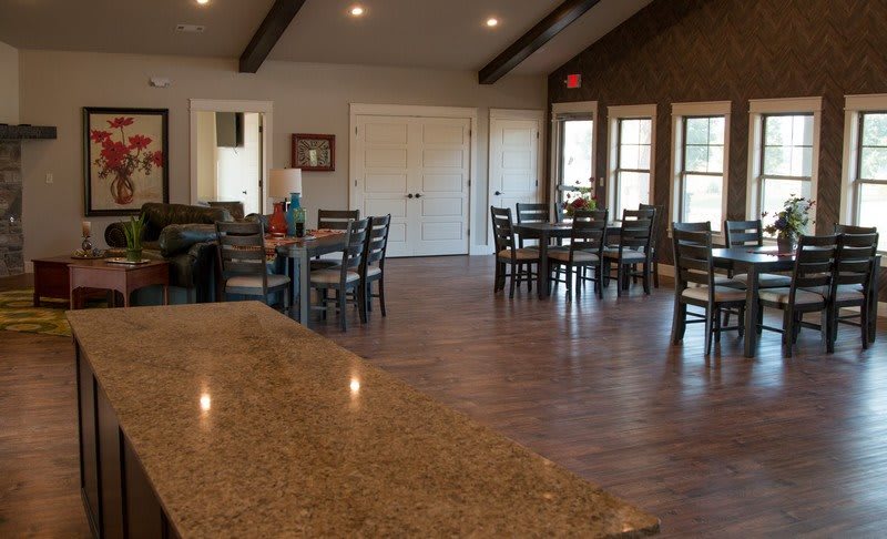 A cozy interior space with a dining area featuring wooden tables and chairs, complemented by large windows and warm lighting.