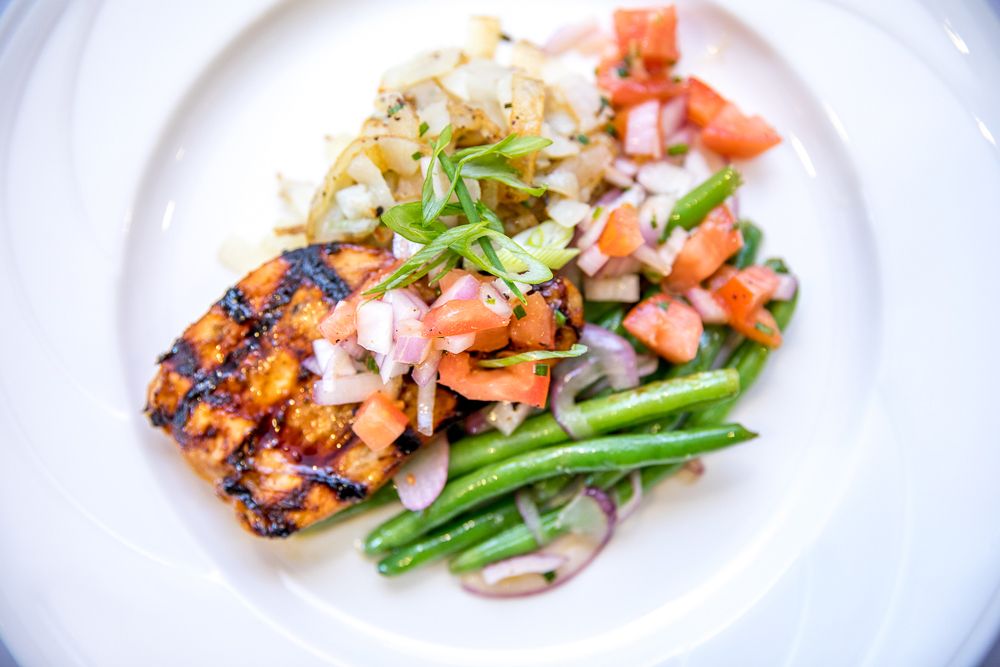 A delicious plate featuring grilled salmon topped with a tomato-onion mixture, served alongside green beans and a roasted potato.