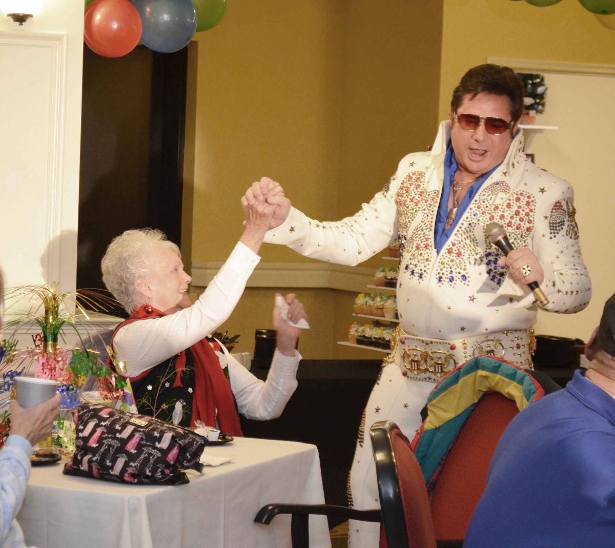 A performer in an Elvis costume entertains a seated guest during a lively celebration.