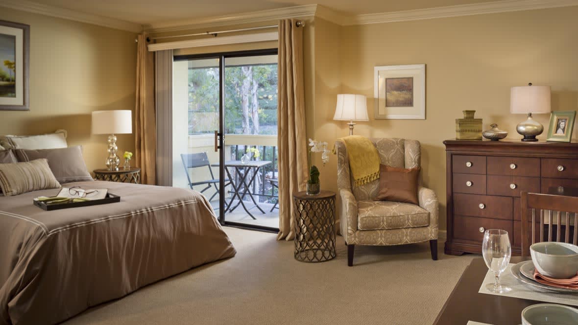 A cozy bedroom interior featuring a comfortable chair, a lamp, and a sliding door leading to a balcony.