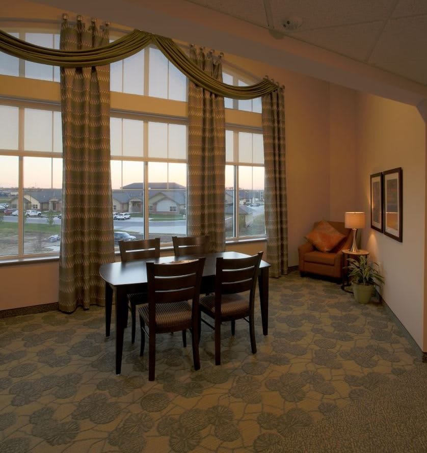 A cozy dining room with a wooden table, chairs, and large windows adorned with curtains.
