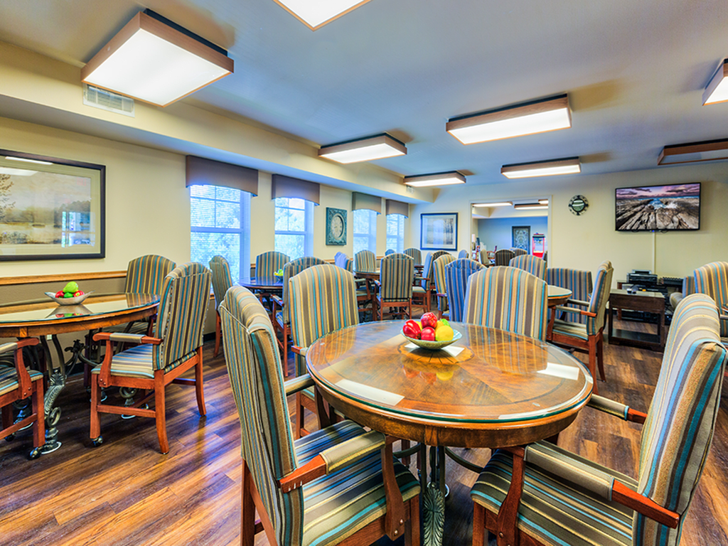 A spacious dining room with multiple tables and chairs, featuring a wooden floor and bright lighting.