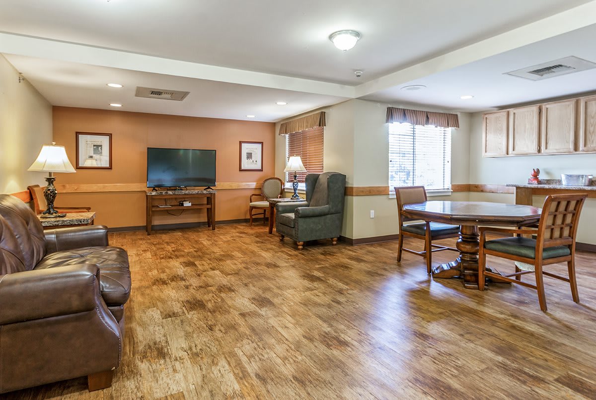 A spacious living room with wood flooring, featuring a television, comfortable seating, and a dining area.