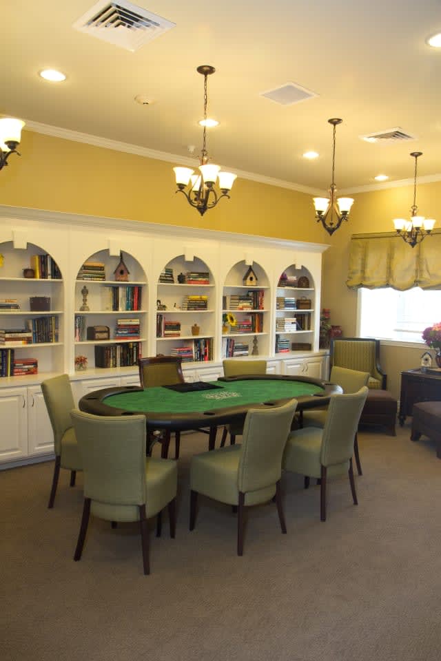 A cozy room featuring a poker table surrounded by chairs, with built-in bookshelves in the background.