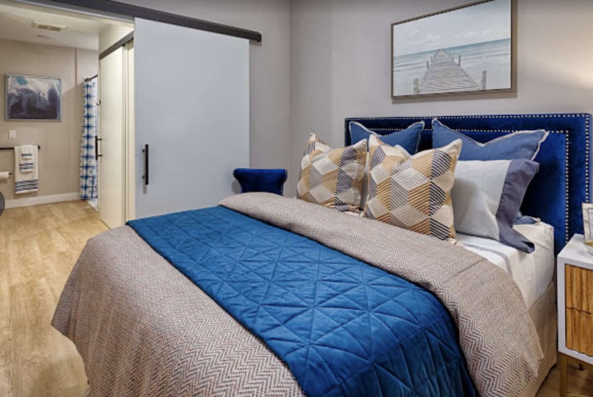 A modern bedroom with a neatly made bed featuring a blue blanket and patterned pillows, complemented by wall art.