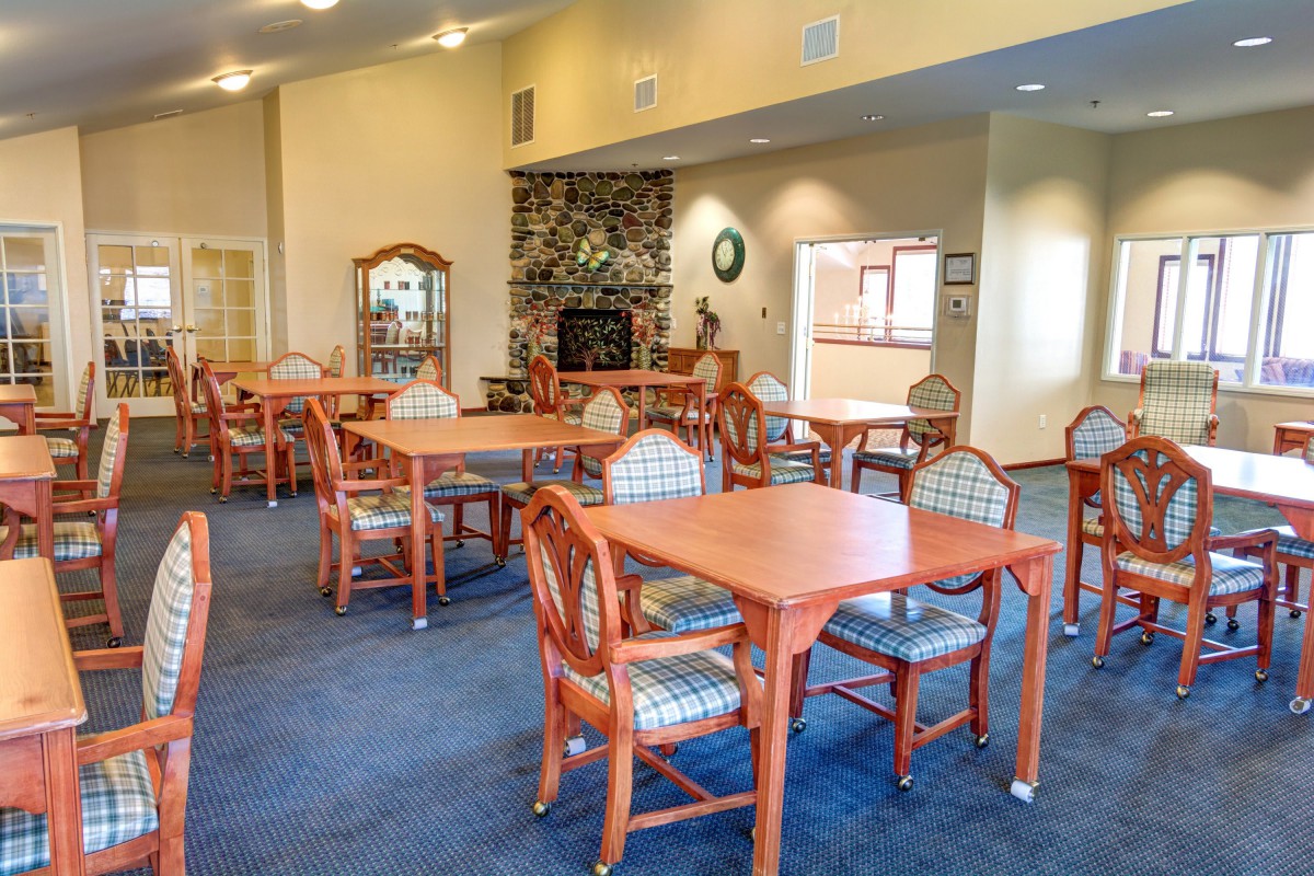 A well-furnished dining room with several wooden tables and chairs, decorated with a carpeted floor and warm lighting.