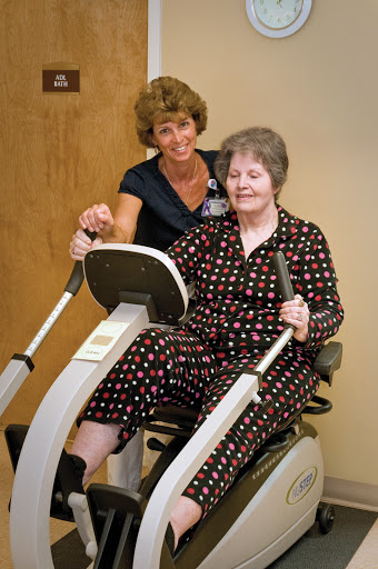 A caregiver assisting an elderly woman on a fitness machine, promoting health and rehabilitation.