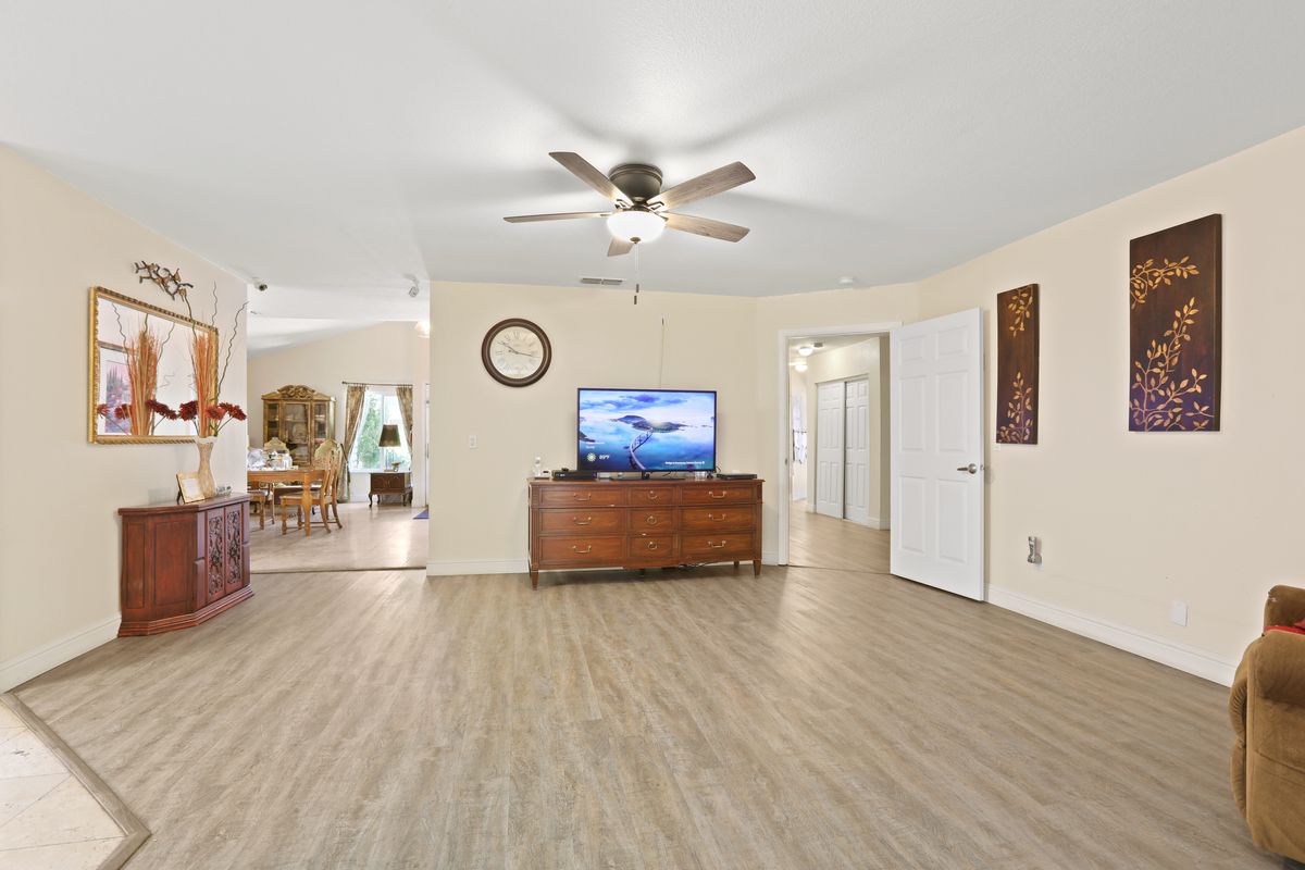 A spacious living room with wooden flooring, a ceiling fan, and a television on a stand.