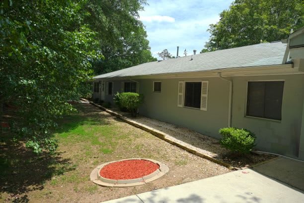 A single-story house with a landscaped yard and surrounding trees.