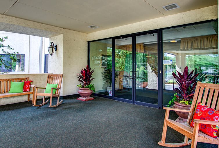 A welcoming entrance area with glass doors, rocking chairs, and potted plants.