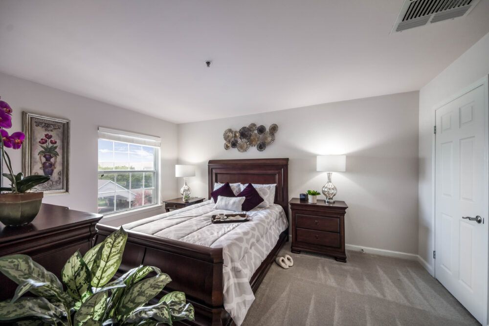A well-lit bedroom with a neatly made bed, wooden nightstands, and decorative elements.
