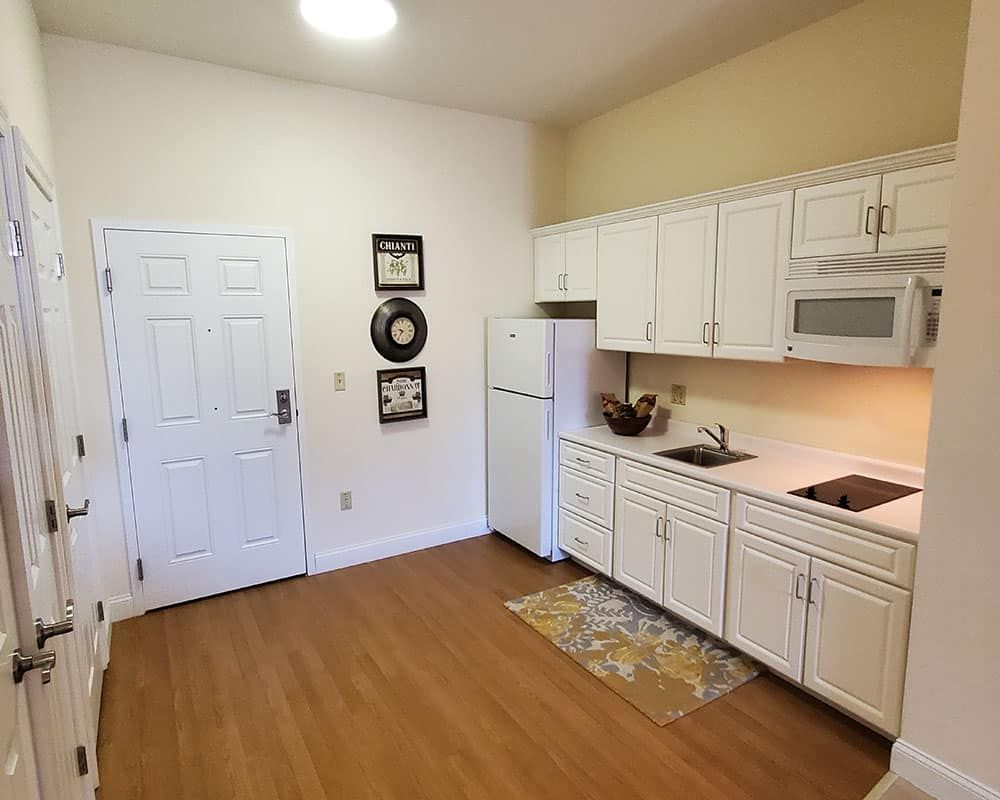 A modern kitchen interior with white cabinets, a fridge, and a microwave on a hardwood floor.