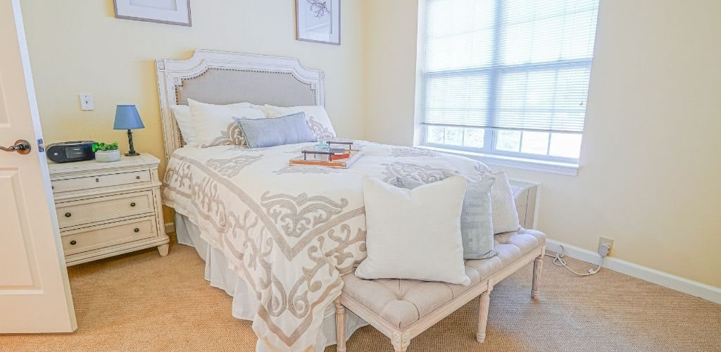 A cozy bedroom with a neatly made bed, decorative pillows, and a bench by the window.