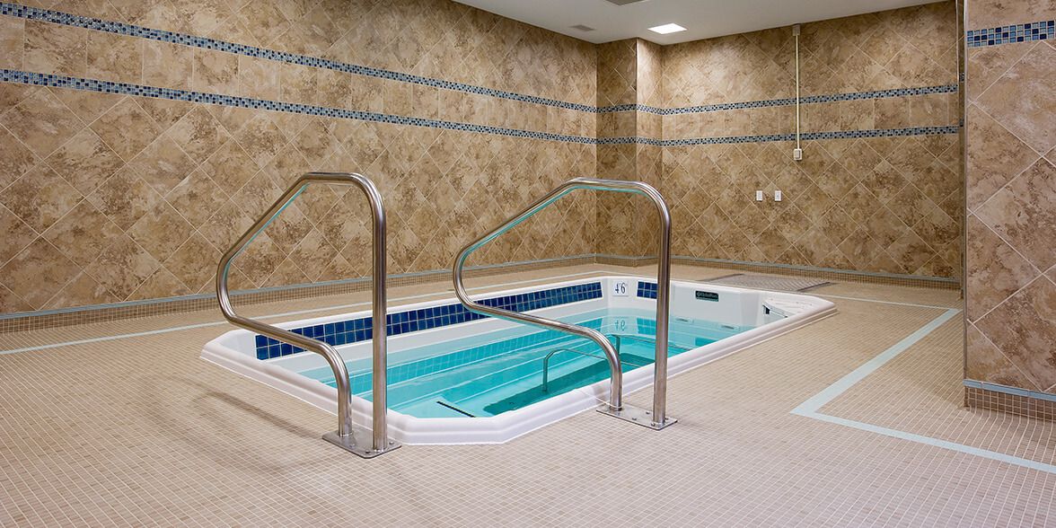 Indoor whirlpool area with tiled walls and safety handrails.