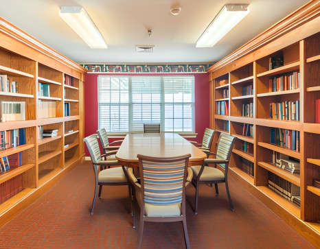 A quiet library room with a large table and surrounding bookshelves, ideal for meetings or study sessions.