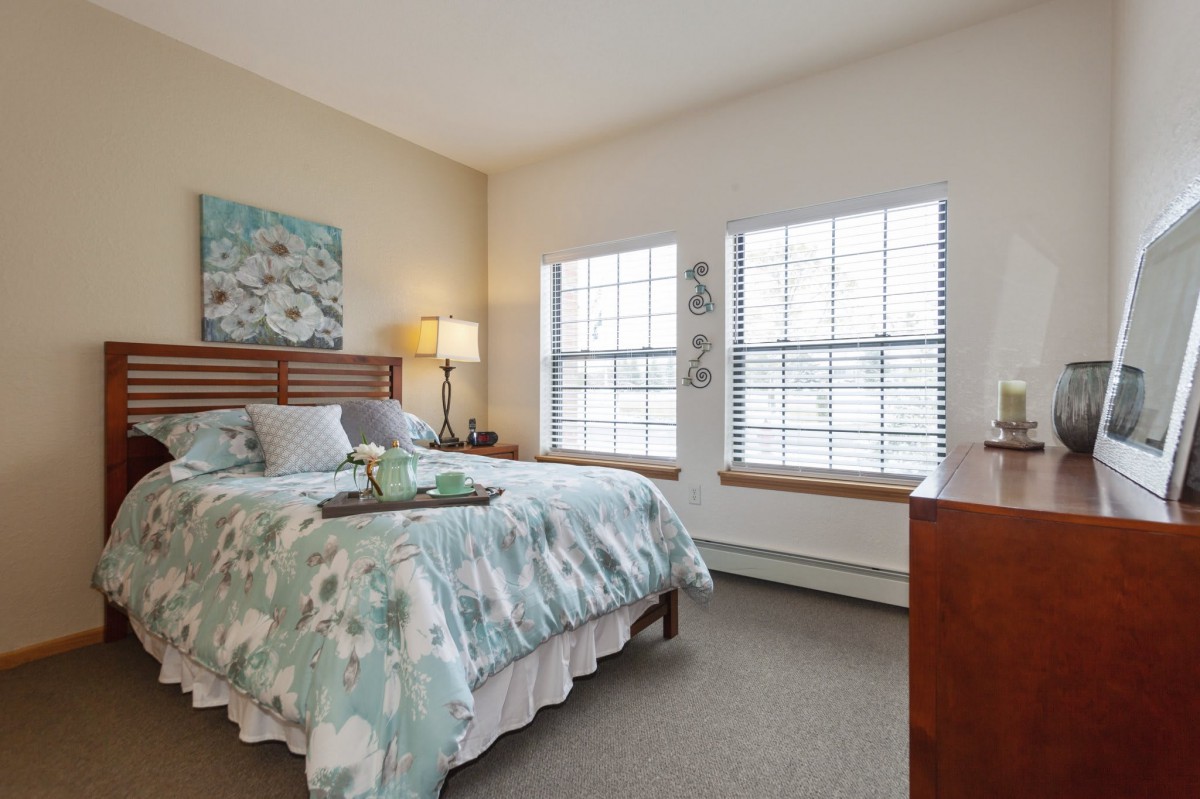 A well-lit bedroom with a cozy bed, floral bedding, and decorative artwork on the wall.