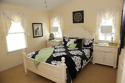 A cozy bedroom featuring a neatly made bed with black and white patterned bedding, flanked by two bedside tables with lamps. The walls are adorned with decorative artwork.