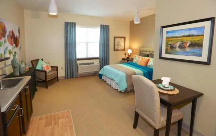 A cozy bedroom with a neatly made bed, chair, and table by the window.