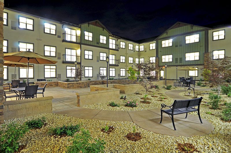 A well-lit courtyard with benches and landscaping in front of a multi-story building at night.