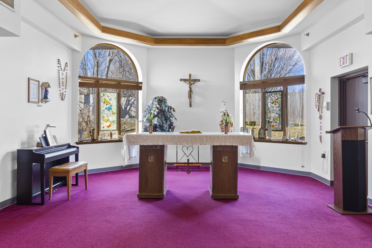 A serene chapel with an altar, featuring a cross on the wall and large windows overlooking a natural view.