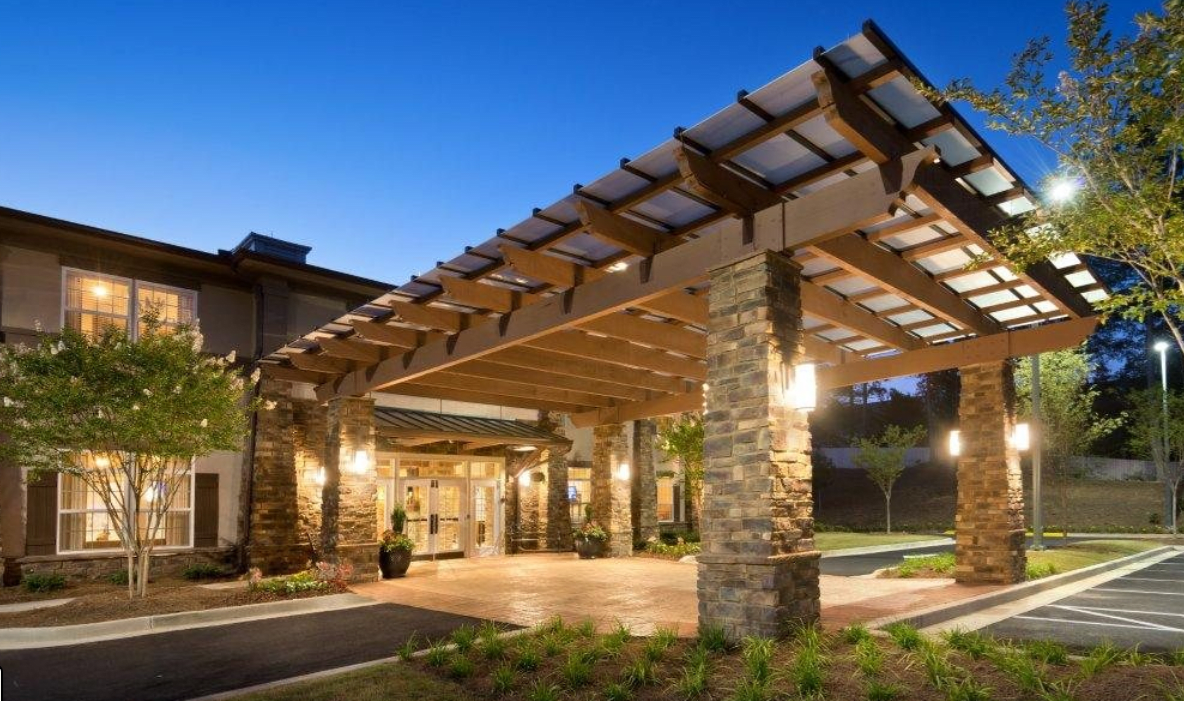 A modern building entrance at night, featuring stone pillars and warm lighting under a wooden canopy.