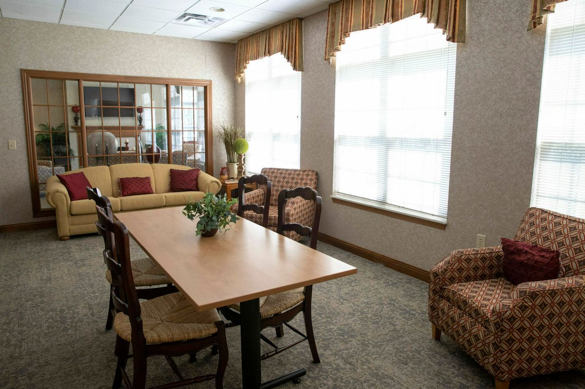 A cozy living room with a table and chairs, a sofa, and large windows with curtains.