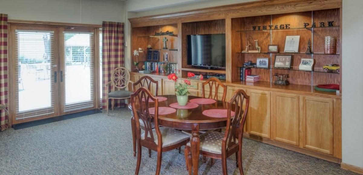 A cozy dining area with a round wooden table, surrounded by chairs and a built-in entertainment center featuring a television and shelves.